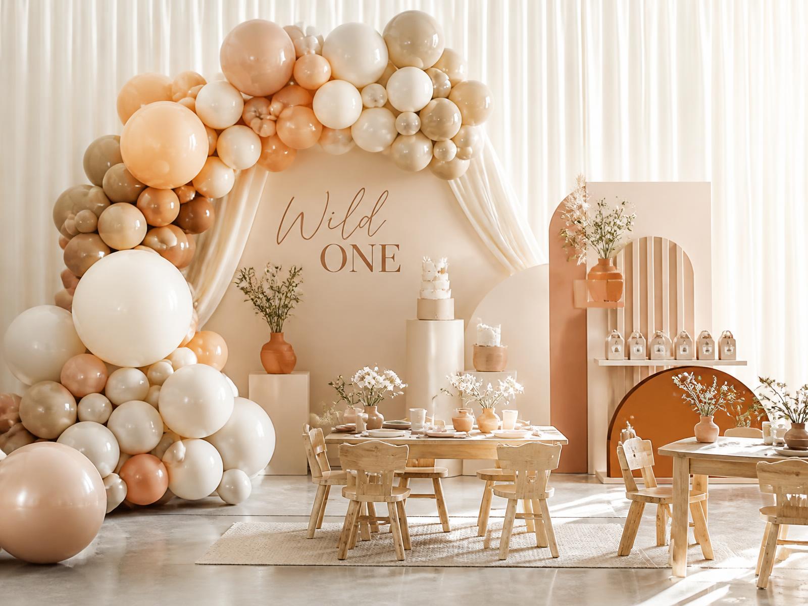 Cumpleaños infantil premium con instalación escultórica de globos en tonos caramelo y mobiliario de madera